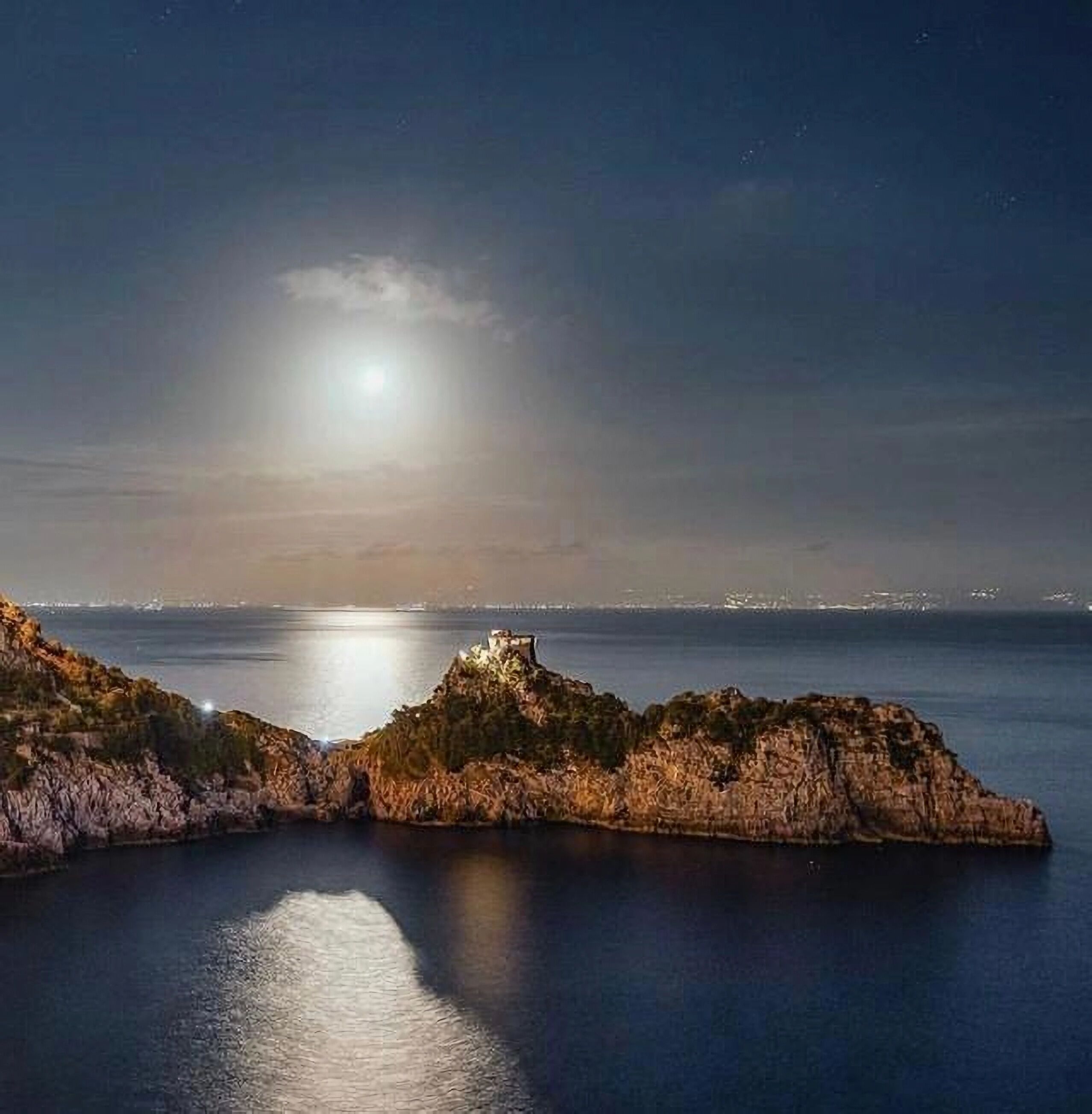 Un paysage côtier caractérisé par des formations rocheuses et des eaux calmes qui reflètent la lumière de la lune.
