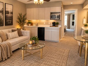 A modern living room with a glass coffee table, a sofa, and a kitchen area with a microwave.