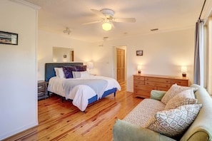 A bedroom with a bed, wooden floor, ceiling fan, dresser, and a nightstand.