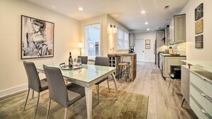 A modern kitchen with a dining area, featuring a glass table, chairs, and a painting on the wall.