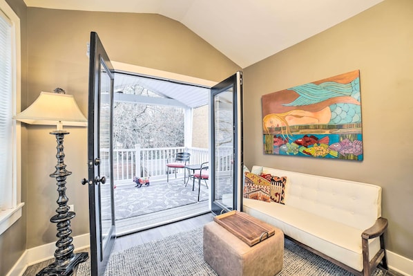A room with a sliding glass door leading to a balcony, a white sofa, a lamp, and a colorful fish painting.