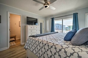 A bedroom with a bed, a ceiling fan, a TV, and a window with curtains. - Holden Beach Vacation Rental: Short Path to Beach! (Holden Beach)