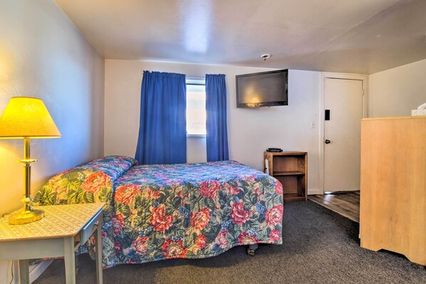 Un dormitorio con cama, escritorio, lámpara, televisor y puerta.