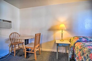 Una habitación pequeña y sencilla con una cama, una mesa, dos sillas, una lámpara y un equipo de aire acondicionado.