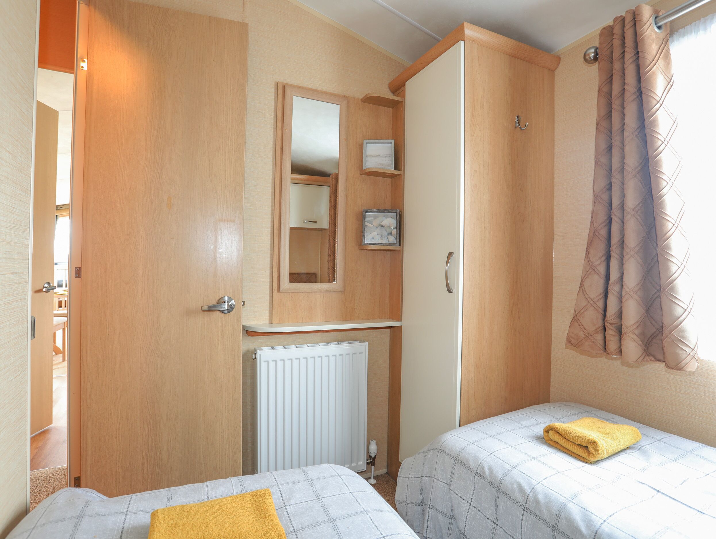 A bedroom with two beds, a radiator, a mirror, and a window with curtains.