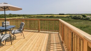 A wooden deck with a table and chairs, overlooking a grassy field. - Mountain View Lodge 2 (Holyhead)
