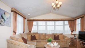 A living room with a sectional sofa, a coffee table, a television, and a large window with curtains. - Mountain View Lodge 2 (Holyhead)