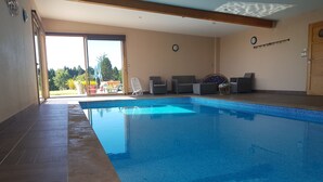 Una piscina interior con suelo de baldosas, tragaluz y vistas al exterior.