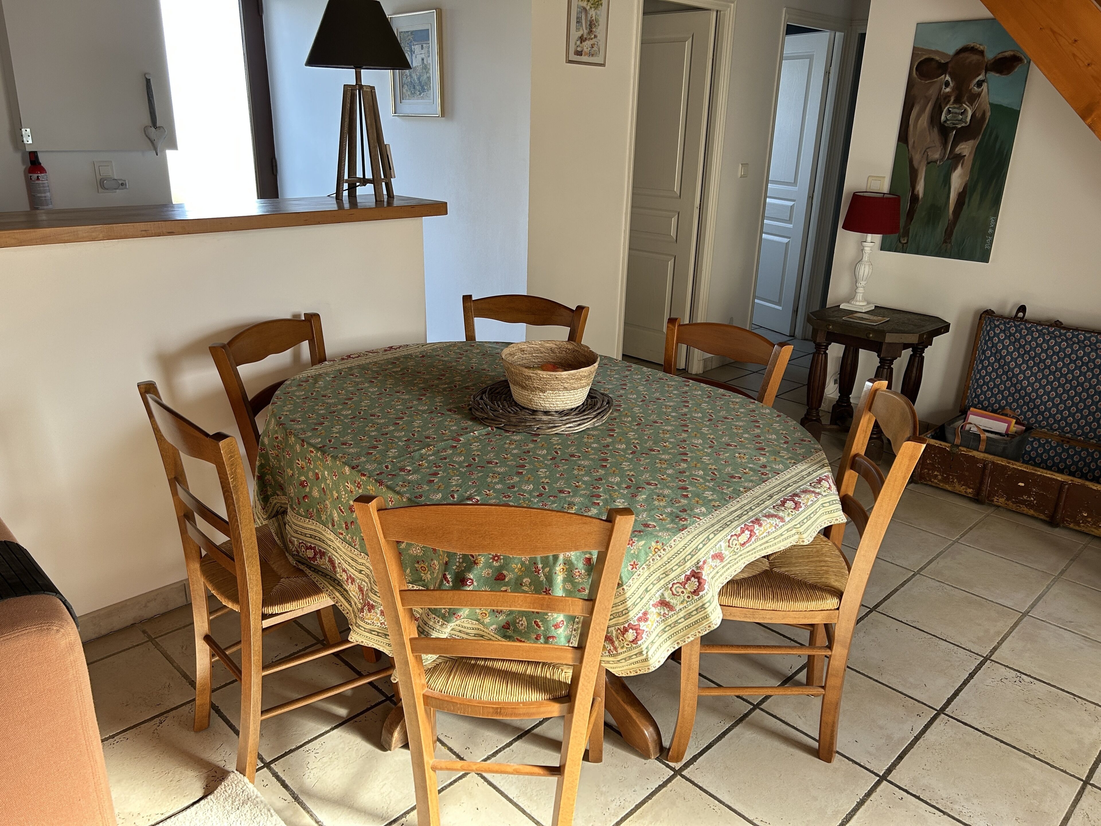 A dining area with a round table covered by a floral tablecloth, surrounded by wooden chairs.