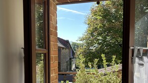 Blick durch ein Fenster auf eine Ziegelwand, einen hölzernen Türrahmen und einen klaren Himmel.