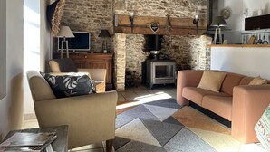 Ein gemütliches Wohnzimmer mit Steinwand, Holzbalken, Kamin, Fernseher und einer Couch.