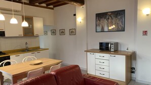 Eine moderne Küche mit weißen Schränken, einer Holz Arbeitsplatte und einer Mikrowelle auf einem Schrank. Es gibt einen Esstisch mit Stühlen und ein rotes Ledersofa.