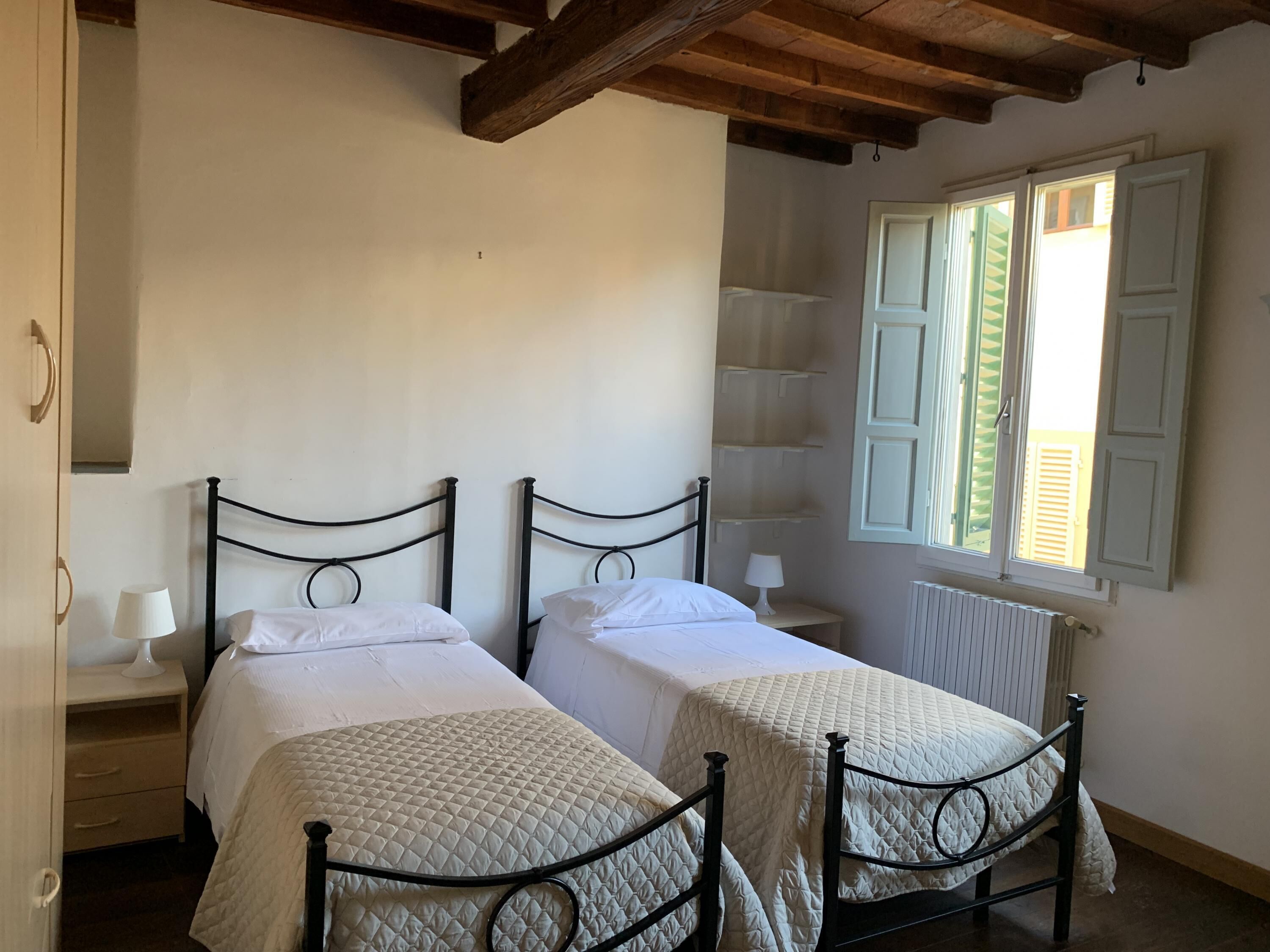 A room with two beds, wooden beams on the ceiling, a window with shutters, and a radiator.