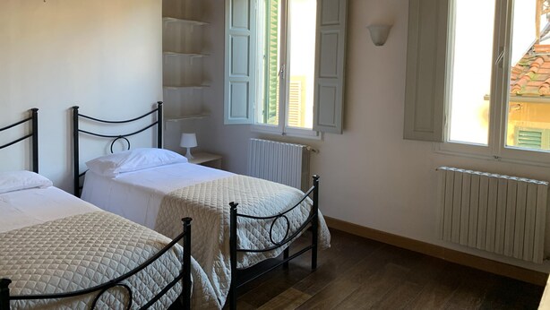 Ein Schlafzimmer mit zwei Betten, Holzbalken an der Decke, einem Fenster mit Fensterläden und einer Heizung.