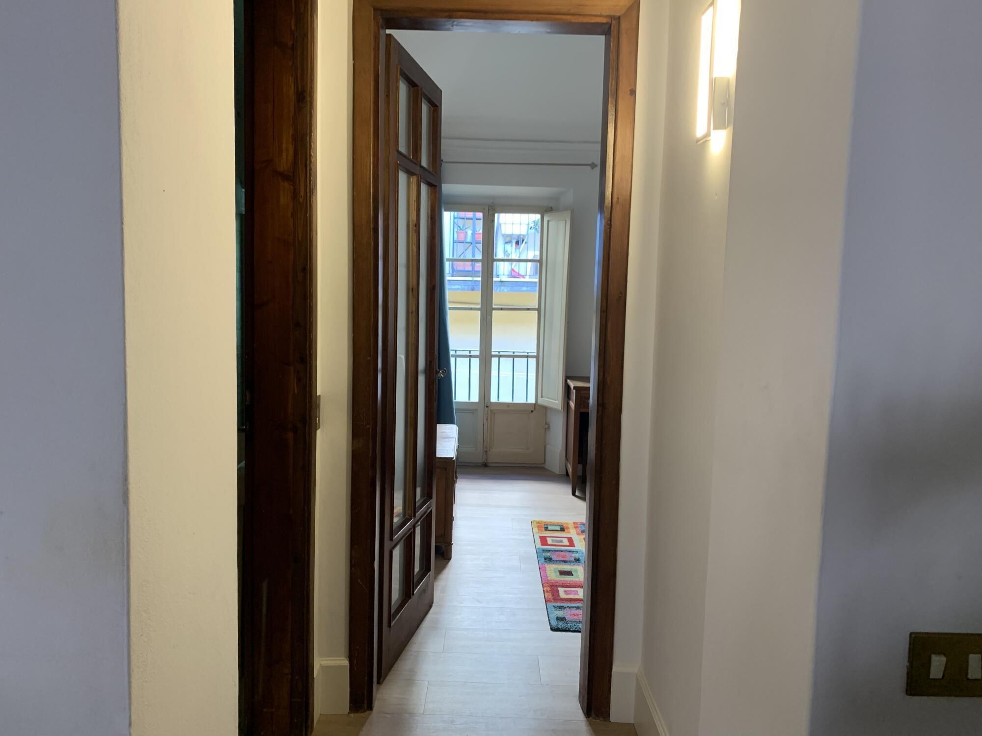 A narrow hallway with wooden doors and a colorful rug on the floor.