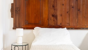 Una cama con ropa de cama blanca, una lámpara de noche y un armario de madera con un panel decorativo.