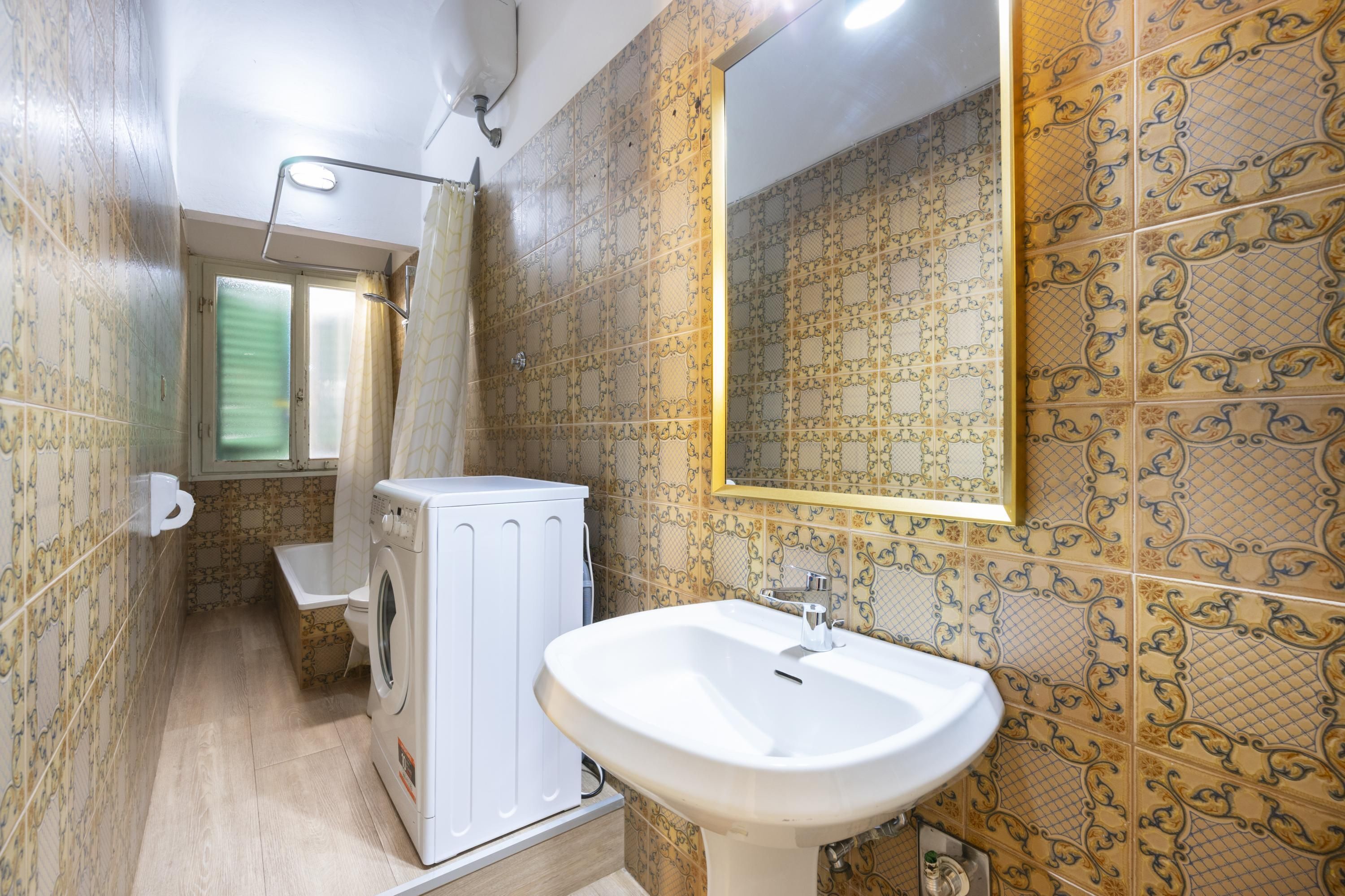 A bathroom with patterned tiles, a white sink, a washing machine, and a mirror.