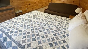 A bedroom with a wooden ceiling, a bed with a patterned quilt, a nightstand, and a dresser.
