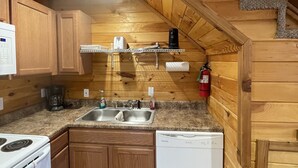 A compact kitchen with wooden walls, a granite countertop, a stove, a dishwasher, and a sink.
