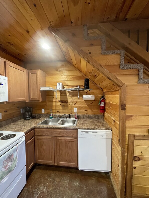 Una cocina compacta con paredes de madera, encimera de granito, estufa, lavavajillas y pileta.