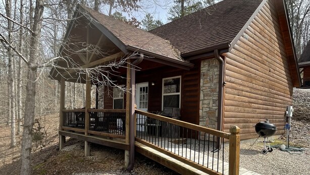 A log cabin with a porch, stone foundation, and a grill outside.