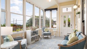 Une véranda avec de grandes fenêtres, un canapé bleu, un fauteuil et une petite table avec une lampe.