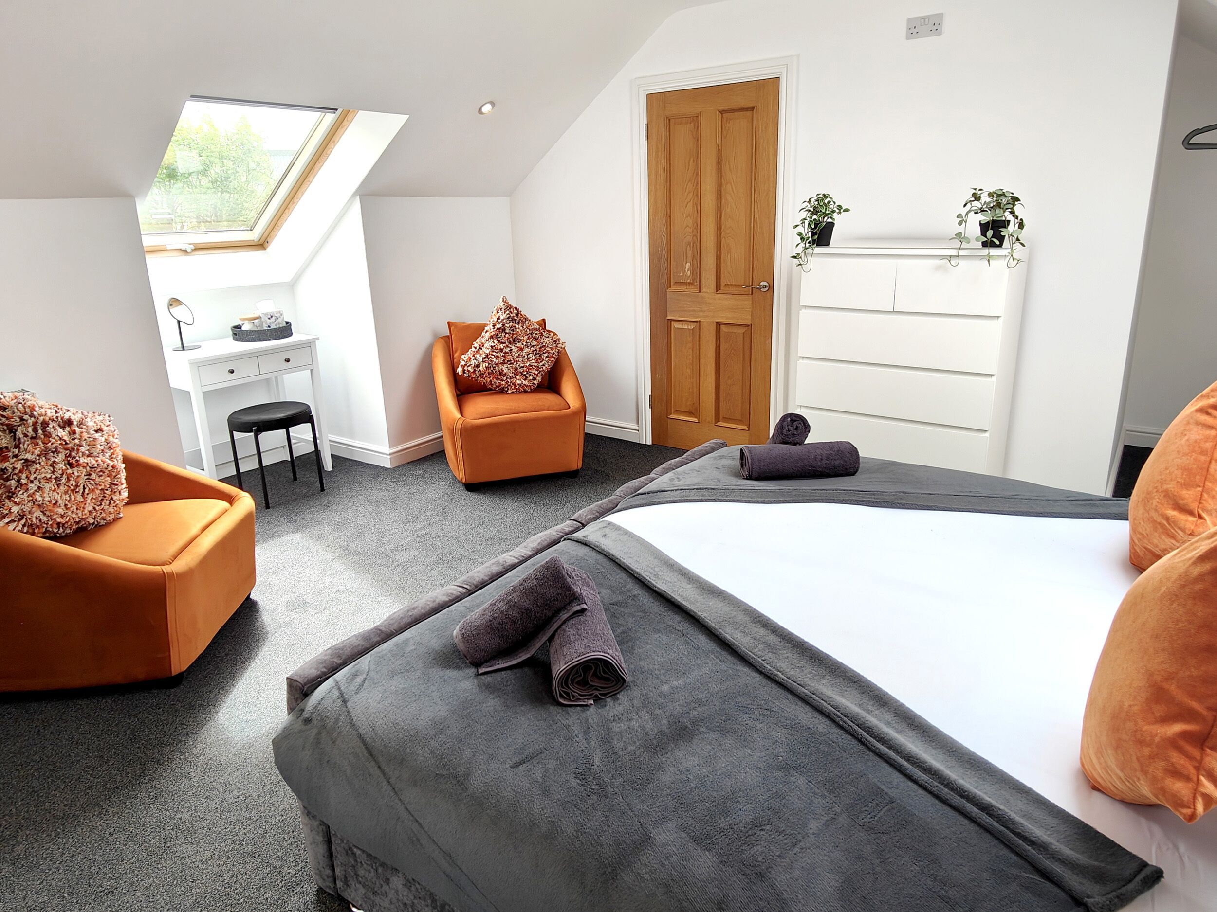 A modern bedroom with a skylight, a desk, a chair, a bed, and a dresser.