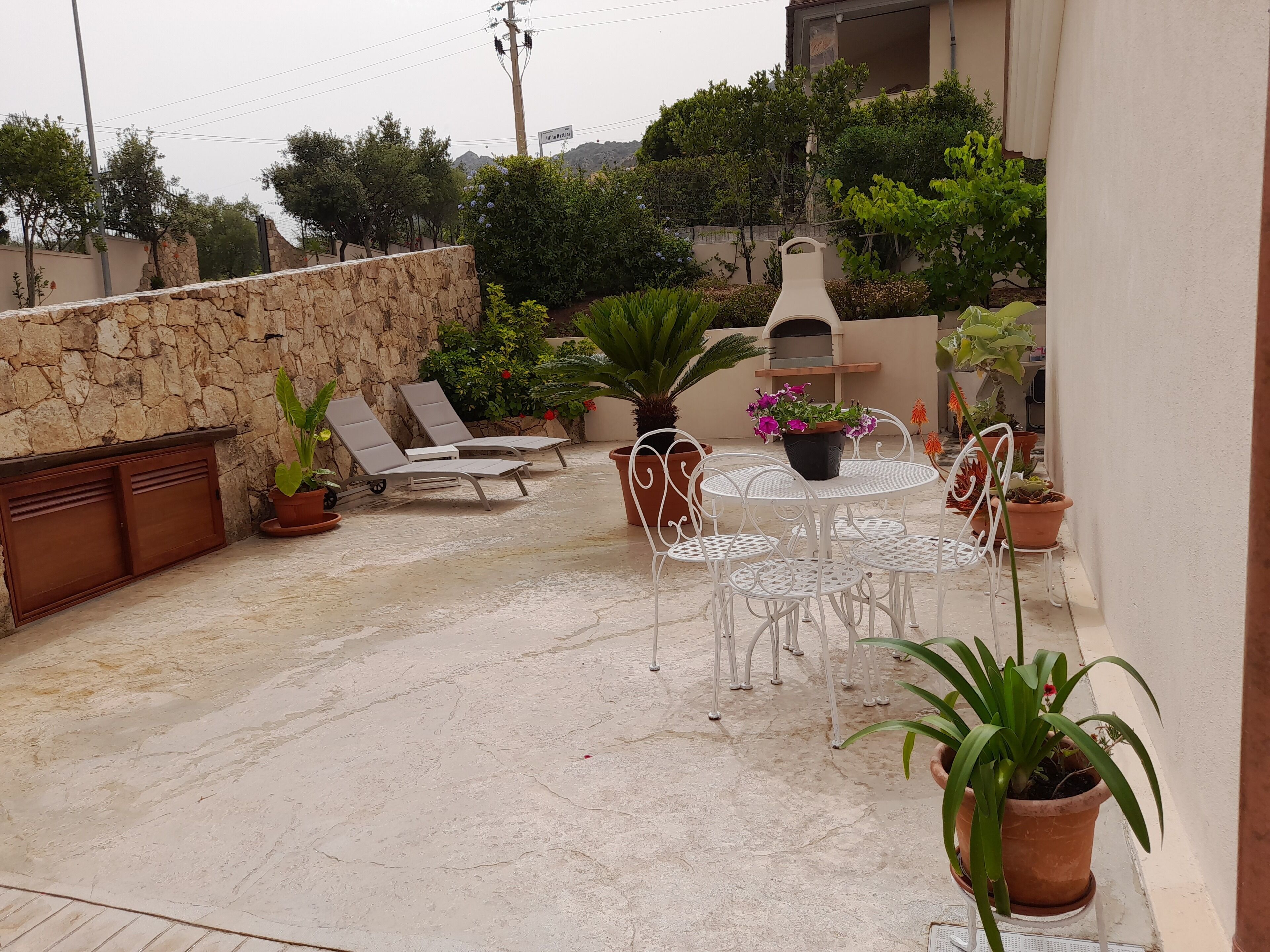 Une terrasse extérieure avec un mur en pierre, un barbecue, des chaises longues et des plantes en pot.
