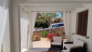 Een kamer met een eettafel, stoelen, een bank en uitzicht op een tuin met een boom en bloemen.