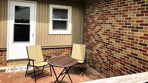 A patio with two chairs and a small table, a white door, and a brick wall.