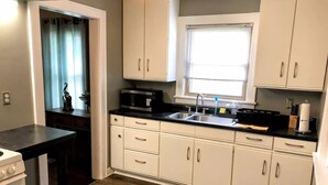 A kitchen with white cabinets, a black countertop, a microwave, and a window with blinds.