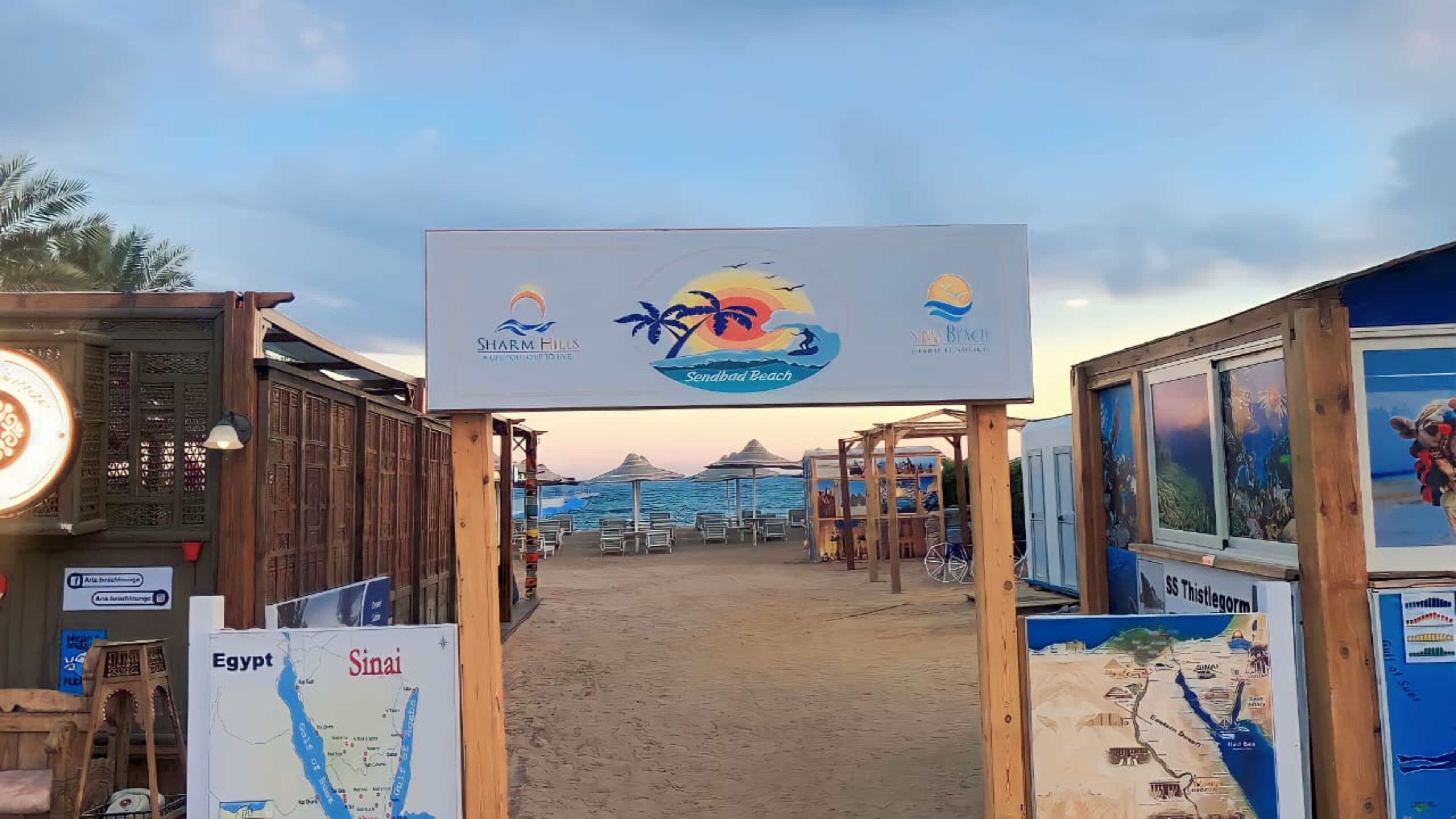 Une promenade en bord de mer avec un panneau indiquant Sharm Hills et Sendbad Beach.