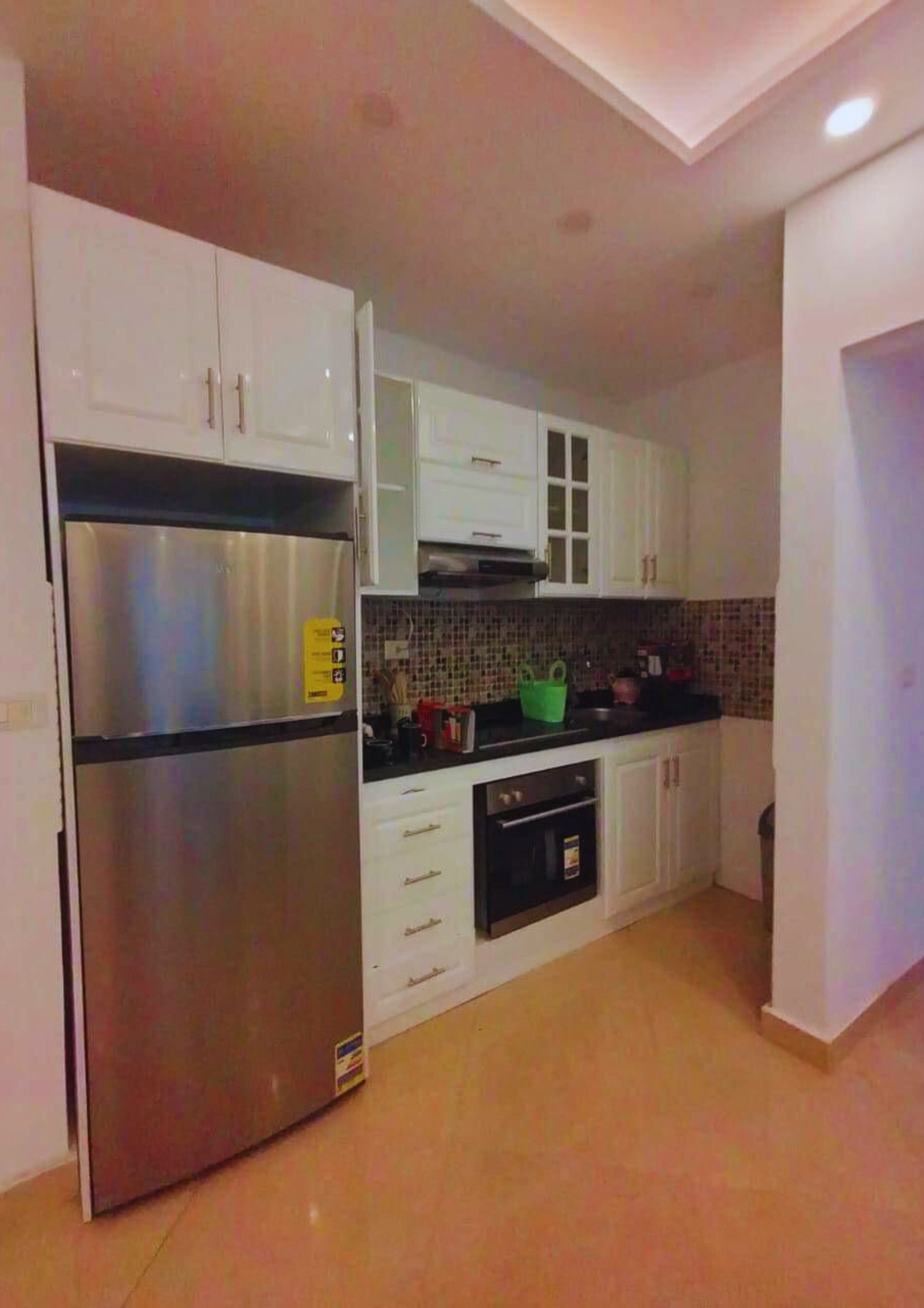 Eine kompakte Küche mit weißen Schränken, einem Edelstahlkühlschrank, einer Mikrowelle und einem kleinen Backofen.