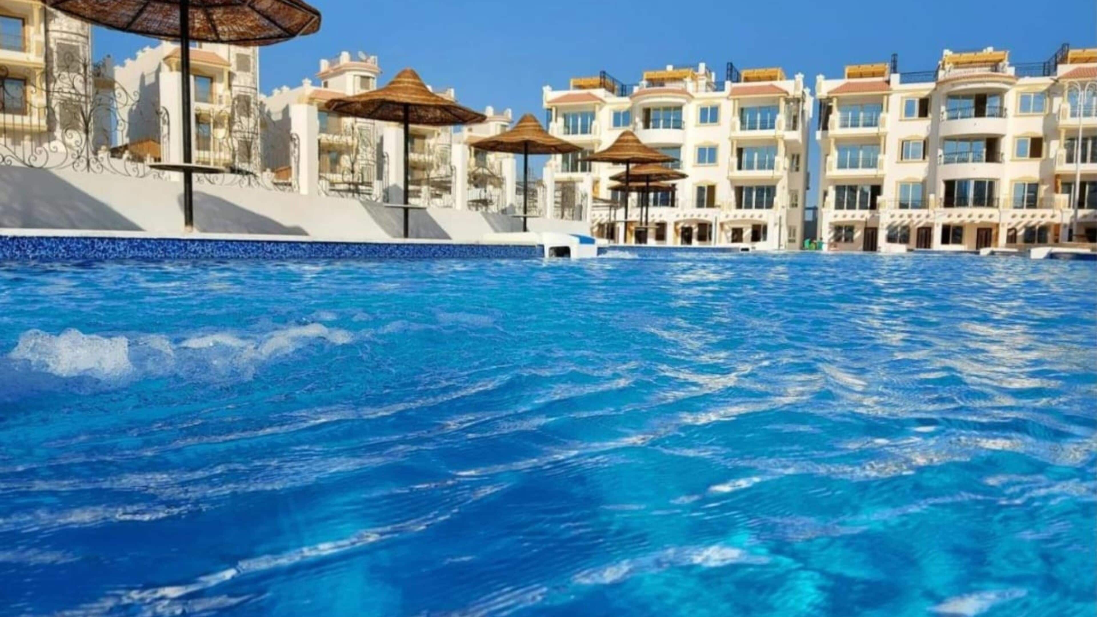 Une piscine à l’eau d’un bleu cristallin, entourée d’immeubles à plusieurs étages dotés de balcons et de parasols.