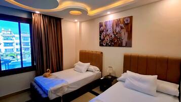 Habitación de hotel con dos camas, un ventanal con cortinas, un cuadro en la pared e iluminación empotrada en el techo.