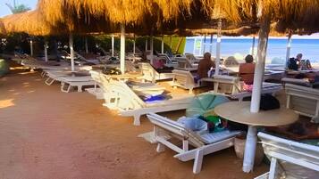 A beachside area with thatched umbrellas and white lounge chairs arranged along the sand.