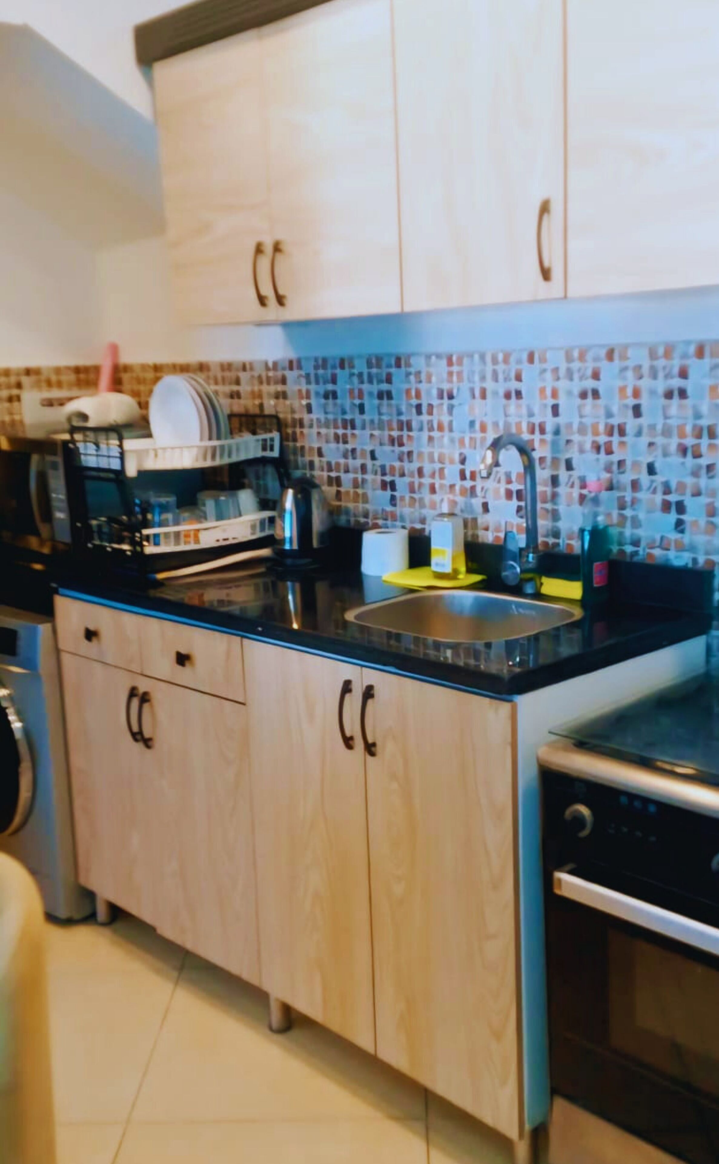 Una cocina con armarios de madera, salpicadero de azulejos, un lavamanos y lavavajillas.