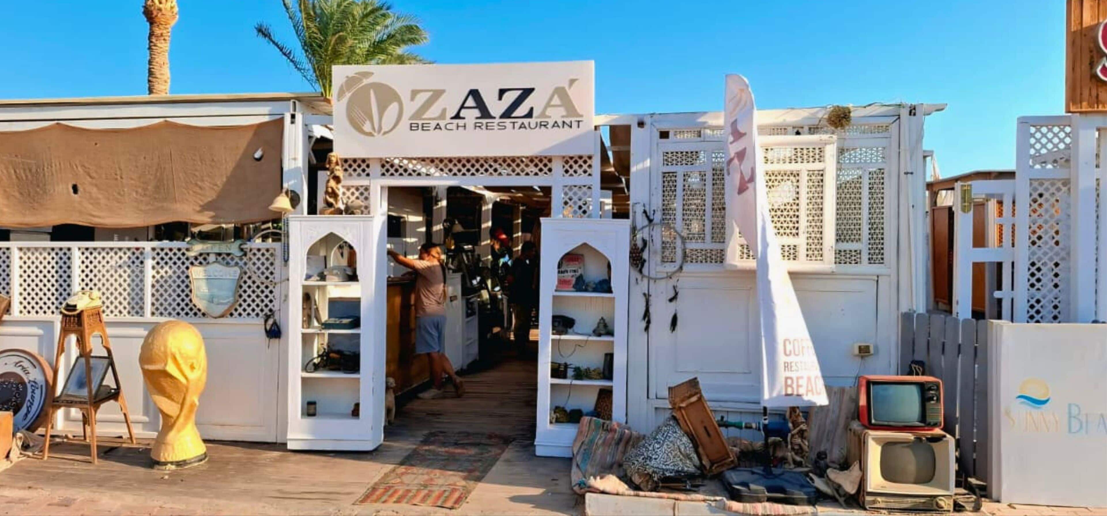 A beach restaurant named 'Zaza' with a traditional architectural style, featuring open shelves and a wooden facade.