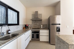 A compact kitchen with a stainless steel refrigerator, built-in oven, granite countertop, and a window with blinds.