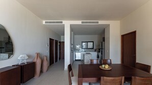 Uma sala de jantar moderna com mesa e cadeiras de madeira, cozinha ao fundo e corredor que dá acesso a outros espaços.