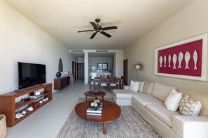 A modern living room with a TV, wooden entertainment unit, round coffee table, beige sofa, and a ceiling fan.