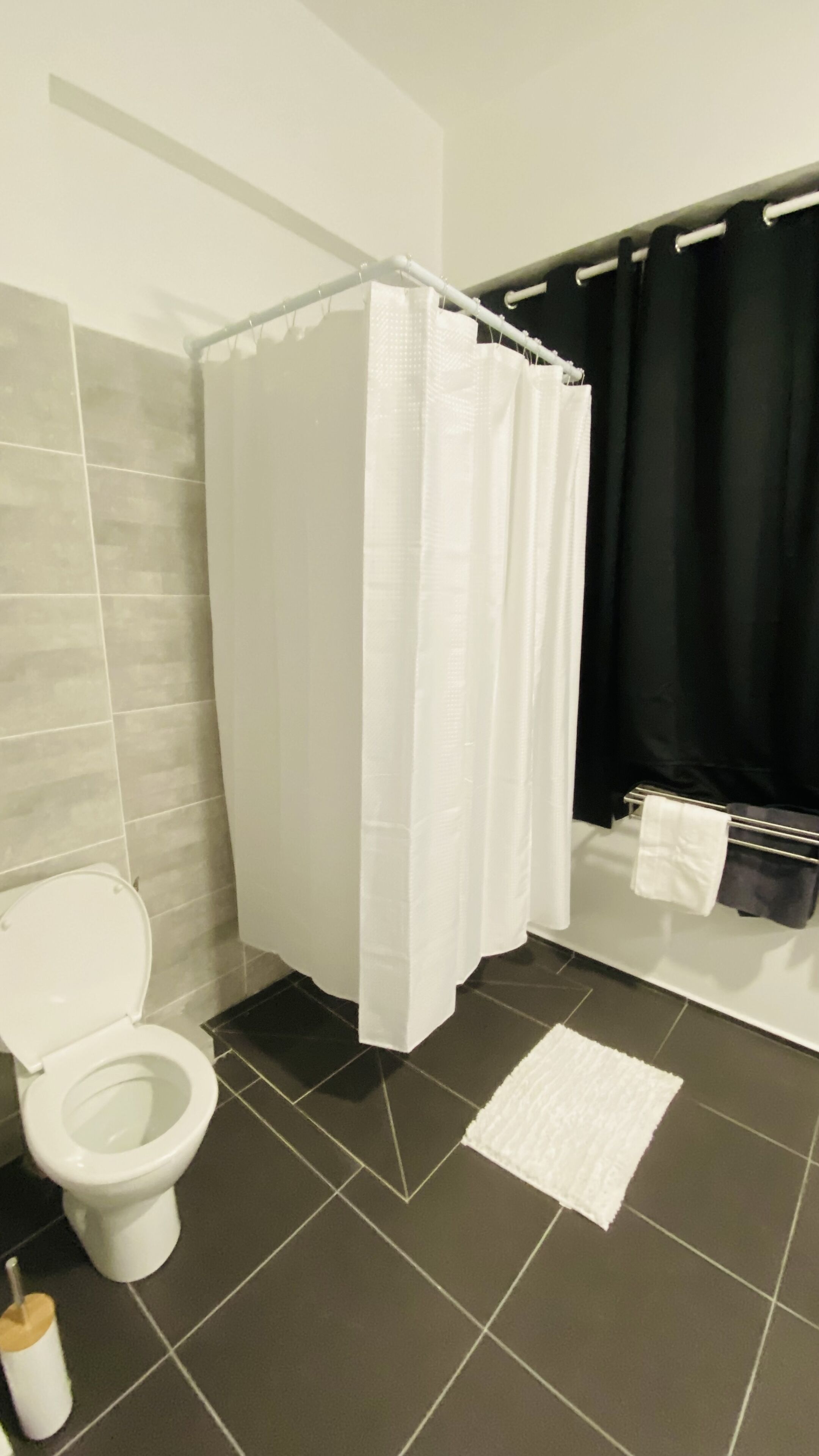 A bathroom with a white toilet, a shower curtain, a towel rack, and a small rug.