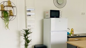 A compact kitchen with a refrigerator, microwave, and a sink with a faucet. There's a trash bin and a potted plant. - Urban Zen Appart in the city center✨ (Pointe-à-Pitre)