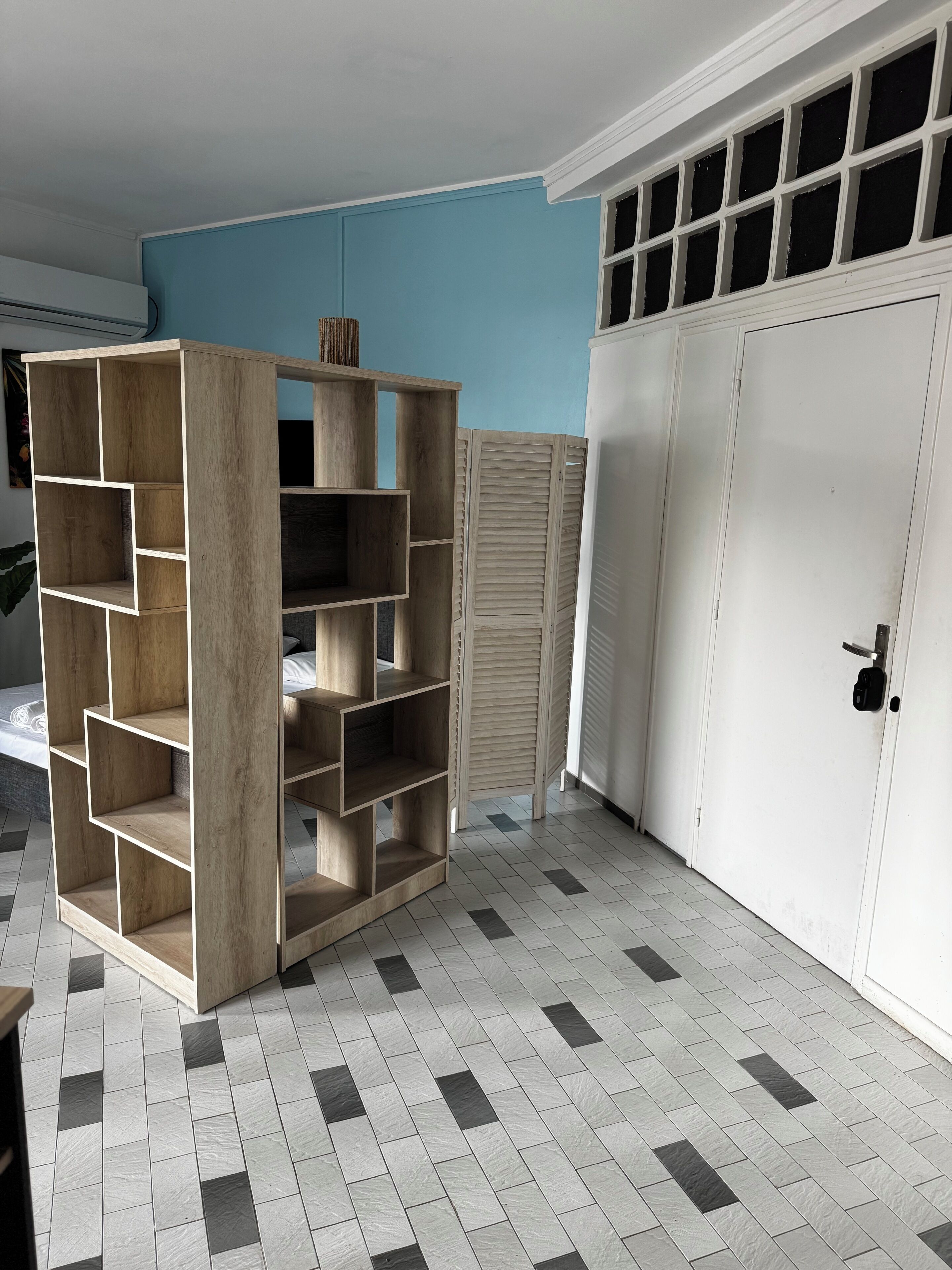 Une pièce avec un sol carrelé, une étagère en bois, une porte blanche et un mur bleu.