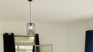 A small dining area with a wooden table, a white chair, a potted plant, and a modern pendant light. - Urban Zen Appart in the city center✨ (Pointe-à-Pitre)