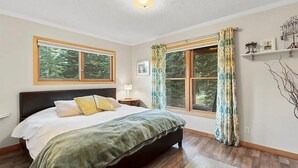 Ein Schlafzimmer mit einem großen Bett, zwei Fenstern, einem Nachttisch und einem Wandregal mit Dekoration.