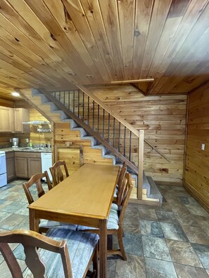A wooden interior with a staircase, a dining table, and chairs.