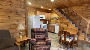 Un intérieur de chalet chaleureux, avec un revêtement mural en bois, un coin repas, une cuisine et un escalier.