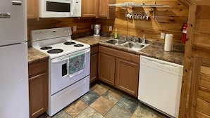 Une cuisine avec des meubles de rangement en bois, un réfrigérateur blanc, un four à micro-ondes, une cuisinière, un évier et un lave-vaisselle.