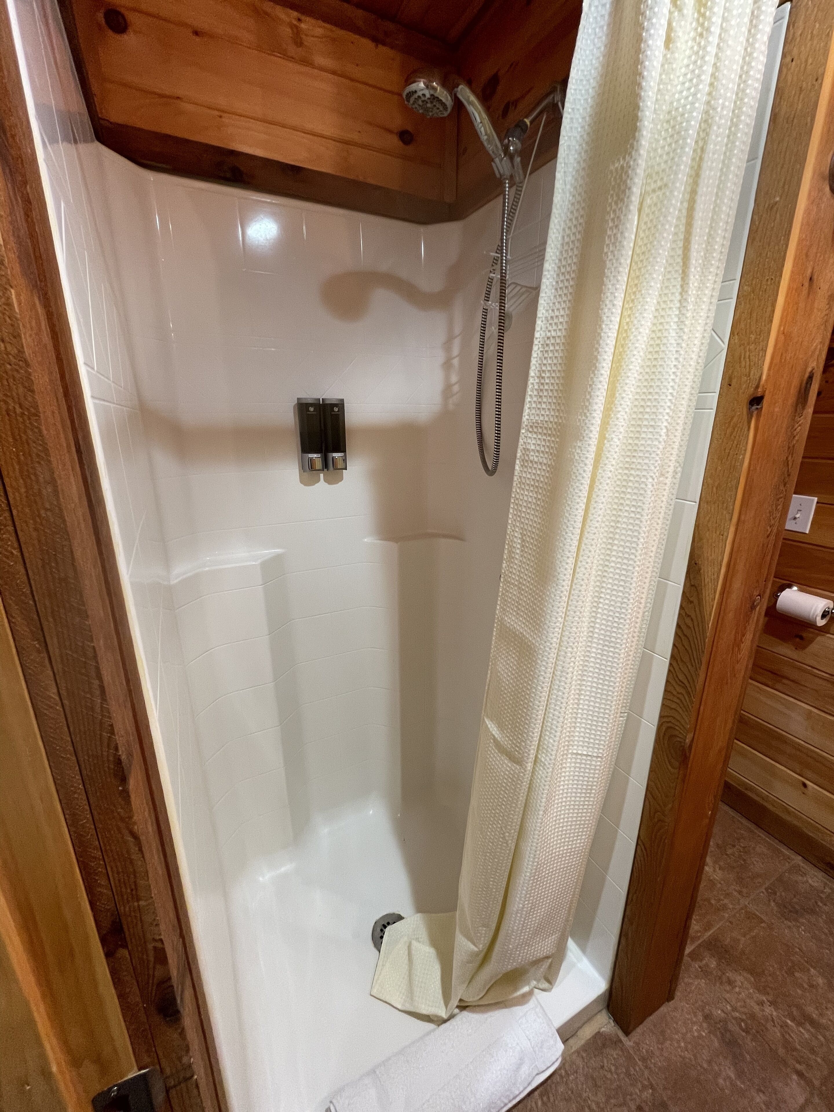Una cabaña de madera con zona de ducha, pared de azulejos blancos, techo de madera y cortina de baño.
